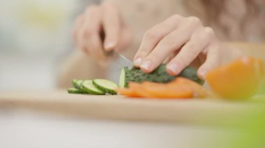 Taze bir salatalığı ustalıkla dilimleyen sağlıklı bir yemek için canlı sebzeleri ön plana çıkaran bir elin yakın plan görüntüsü.