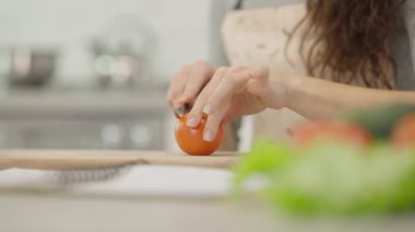 Yetenekli bir insan, modern bir mutfak alanında iyi işlenmiş bir ahşap kesme tahtasıyla olgun bir domatesi ustalıkla dilimliyor.