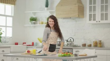 Kadın şarkı söyler, dans eder ve modern bir mutfakta çeşitli taze ve renkli malzemeler hazırlar..