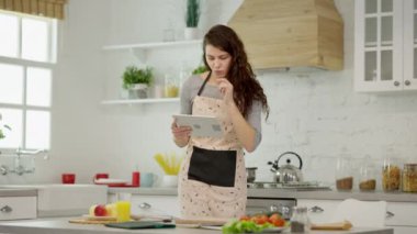 Bir kadın, ailesi için sağlıklı ve lezzetli yemekler hazırlarken modern mutfağında tablet kullanıyor.