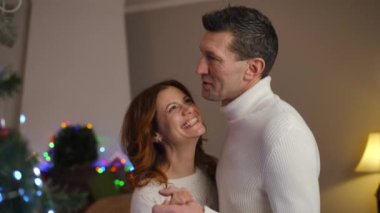 Ağır çekim. Sevgi dolu bir çift, Noel ağacının hemen yanında, bayram sezonunda keyifli ve sıcak bir anı paylaşır.