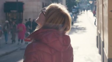 Sıcak, yastıklı bir ceket giymiş, güneşin öptüğü bir caddede yürüyen ve günün tadını çıkaran birinin arka görüntüsü.