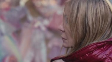 Derin düşüncelere dalmış bir kadın, kar taneleri hafifçe parıldıyor saçlarının arasında, canlı şehir sanatıyla çevrili.