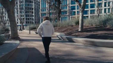 Bir kadın, çarpıcı modern binalar ve bereketli doğa ile çevrili canlı bir şehir parkında rahatça dolaşır.