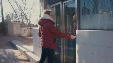 Güneşli güzel bir günde genç bir kadın parlak kırmızı bir ceket giyerek cam kapıya doğru yürüyor.