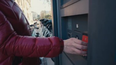 Canlı ve hareketli bir şehir manzarasında, bir kişi hareketliliği artıran bir ebike kiralama kioskuyla temas kurar.