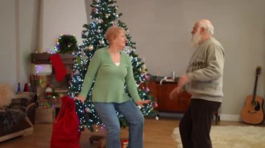 Güzel dekore edilmiş bir Noel ağacının yanında neşeyle dans eden yaşlı bir çift rahat evlerindeki şenlikli ruhu kucaklıyor. Ilık bir ışık ve neşeli bir atmosfer yaratıyor.