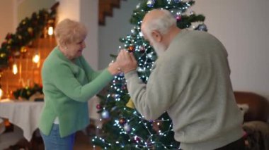 Yaşlı bir çift Noel ağacını neşeyle süslüyor, tatil sezonunun ruhunu yakalıyorlar..