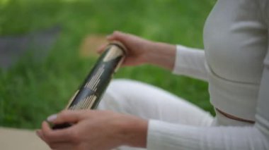 Huzurlu bir parkta meditasyon seansı sırasında rahatlatıcı ritmik sesler yaratmak için bir yağmur çubuğunu tutan ve eğen ellerin yakın çekim görüntüsü. Katılımcı beyaz giyer ve alıştırmaya zarafet katar.