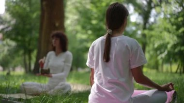 İki kadın huzur parkında meditasyon yapıyor. Biri sırtını pembe yoga minderine yaslamış, uzun saçı arkadan bağlanmış, diğeri ise Tibet şarkı kasesini tutuyor. Beyaz elbiseleri.