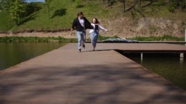 Neşeli bir çift yavaş çekimde sakin bir gölün kıyısında ahşap bir rıhtımda el ele koşuyor. Kaygısız ifadeleri ve neşeli enerjileri sıcak güneş ışığı altında neşeli bir an yaratıyor.