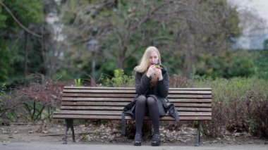 Genç bir kadın sakince bir bankta oturuyor, sakin bir parkta, elinde renkli bir oyuncağa odaklanmış.