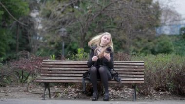 Zarif siyah bir palto giymiş bir kadın zarif bir park ortamında duruyor, sükunet ve güzellik sergiliyor.