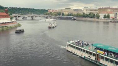 Prag, Çek Cumhuriyeti, 27 Haziran 2023: Timelapse arka planda ikonik köprüler ve tarihi mimariyle Vltava Nehri boyunca seyreden tekneleri yakalıyor. Videoda hareketli bir nehir var.