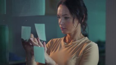 Çağdaş bir ofis ortamında, bir kadın dikkatle ve dikkatlice çeşitli yapışkan notları inceler.