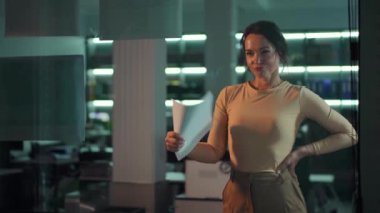 Zarif, modern ofis ortamında odaklanmış ve azimli bir kadın çalışırken elinde bir belge tutuyor..