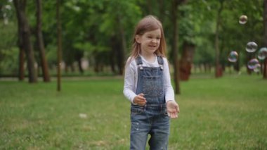 Tatlı ve neşeli genç bir kız güzel yeşil bir parkta mutlu bir şekilde duruyor, saf masumiyet ve neşe saçıyor.