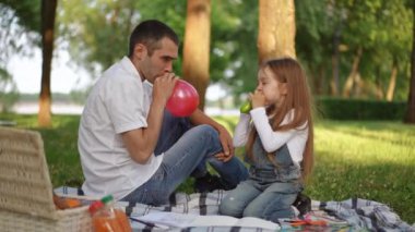 Mutlu bir baba ve küçük kızı, gülücüklerle dolu, güneşli bir parkta pikniğin tadını çıkarıyorlar.