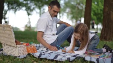 Sevgi dolu bir baba ve kızının yemyeşil bir parkta sanattan keyif aldığı canlı ve neşeli bir piknik sahnesi.
