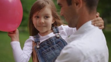 Sevgi dolu bir baba, genç kızını güzel, yemyeşil bir parkta parlak bir balonla mutlu bir şekilde tutar.