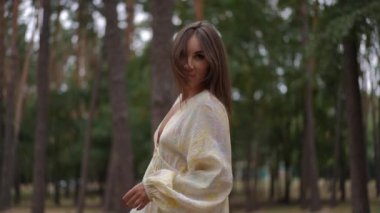 Keratin açısından zengin, uzun, parlak saçları olan ve huzurlu bir ormanda vitaminlerin omzunun üstünden baktığı bir kadın. Pürüzsüz, beslenmiş iplikleri en uygun hidrasyon ve özeni yansıtıyor.