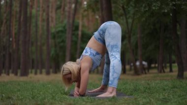 Bir kadın dışarıda yoga yapıyor, dingin bir orman ortamında etkileyici esnekliğini ve sakinliğini gösteriyor.