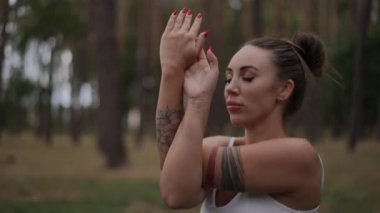 Huzurlu bir ormanda yoga sırasında kartal kolu pozu veren bir kadının yakın çekimi. Odaklanmış ifadesi, enerjik dövmeleri ve kırmızı tırnakları huzur sahnesine eşsiz bir dokunuş katıyor.