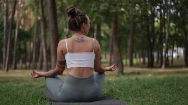 Bir kadın, huzurlu bir ormandaki yoga minderinde meditasyon yapan bir nilüferde poz verir. Sırtının üstündeki kuş dövmesi özgürlüğü ve zarafeti sembolize ediyor, sakin ve odaklanmış tavrını tamamlıyor. Giyinik.