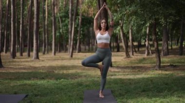 Sakin, sakin bir ormanda yoga yapan bir kadın dengesini ve farkındalığını ön plana çıkarıyor.