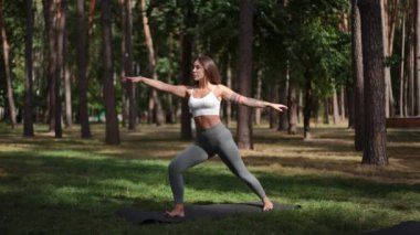 Genç bir kadın, huzurlu bir orman ortamının huzurlu güzelliği içinde çeşitli yoga pozları vermenin keyfini çıkarıyor.