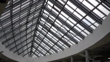 Metal bir iskelet tarafından desteklenen geniş üçgen cam tavanlı bir alışveriş merkezinin içi. Tasarım modern ve minimalist estetiği vurguluyor. Beyaz duvarlar ve sütunlar güçlendirir