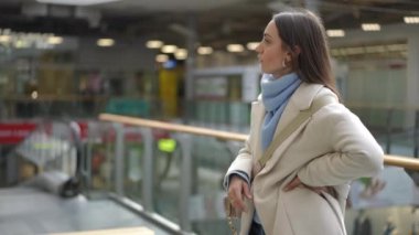 Uçuşlarına geç kalan bir kadın, telaşlı bir havaalanı terminalinde endişeyle kocasını bekliyor. Parlak renkli, gümrüksüz hediye çantalarıyla geliyor.