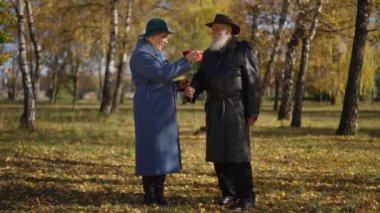 Huzurlu bir sonbahar parkında duran yaşlı bir çiftin dokunaklı sahnesi. Adam, elinde kalp şeklinde bir nesne tutarken sıcacık gülümseyen kadına tek bir kırmızı gül uzatıyor. Bu romantik jest