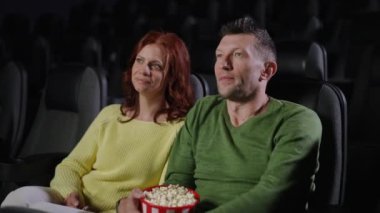 Çift sinemada sıcak bir anın tadını çıkarıyor, filmi izlerken gülüyor ve patlamış mısır paylaşıyor. Adam şakacı bir şekilde kadına bir parça patlamış mısır sunuyor ve neşeli bir anı paylaşıyorlar.