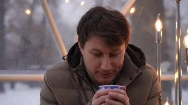 Karlı bir arazide sıcak bir içeceğin tadını çıkaran bir adam bu sakin mevsimde kış rahatlığının özünü yakalar.
