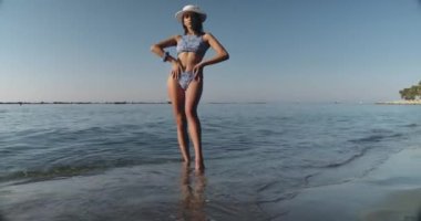 Kıbrıs 'ın Limasol kentindeki Akdeniz' in kumlu sahillerinde güzel bir model poz veriyor. Şık bir mayo ve şapka giymiş, açık mavi gökyüzü ve açık denizde kendine güvenen bir poz sergiliyor.