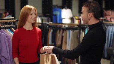 Bir butik çalışanı, alışveriş çantasını alırken memnun bir müşteriye sıcak bir şekilde sarılır. Gülümseyerek, harika bir alışveriş deneyiminden sonra mağazadan neşeli bir şekilde ayrılıyor, mükemmel bir müşteriyi yansıtıyor.