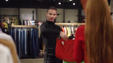 Gösterişli siyah kıyafetli bir stilist butikte moda yeşil ve turuncu etekler arasında seçim yapmasına yardımcı olur. Dostça etkileşimde uzman moda tavsiyeleri ve tarz tutkusu sergileniyor