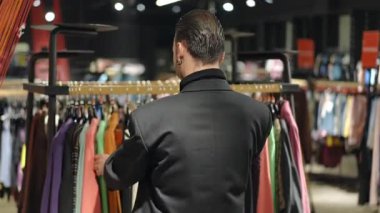 LGBT topluluğundan siyah ceketli bir adamın giyim mağazasında renkli kıyafetlere baktığını gördüm. Doğru giysiyi bulmak için seçmelere göz atıyor.
