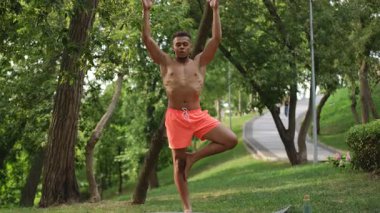 Bir adam etrafını saran yemyeşil bolluk içinde zorlu dengeleyici bir yoga pozu sergiliyor.