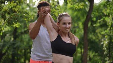 Korkulu yoga eğitmeni, parkta esneme egzersizi yapan genç bir kadına yardım ediyor. Gülümsüyor ve antrenörden destek alıyor, o da ona yol gösteriyor. Sahne hazır.