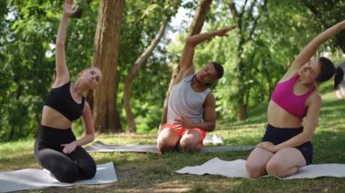 İki kadından oluşan bir yoga grubu ve bir yoga eğitmeni parkta esneme hareketleri yapıyor. Katılımcılar esneklik ve esneme pratiği yaparken eğitmenlerin hareketlerini takip ederler.