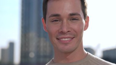 Neşeli ve neşeli bir adam, canlı bir şehir siluetine karşı güvenle gülümsüyor.