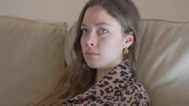 Genç bir kadın rahat mekanında huzur içinde oturur. Etrafındaki huzurlu ve rahat atmosferi derinden yansıtır.