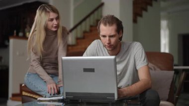 Bir çift sıcak ev ortamında özenle bir dizüstü bilgisayar üzerinde çalışırken aktif bir şekilde tartışır.