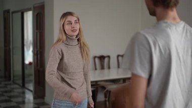 İki birey arasındaki gergin ve yüklü bir etkileşim yumuşak bir şekilde aydınlatılmış, modern bir iç mekanda gerçekleşir.