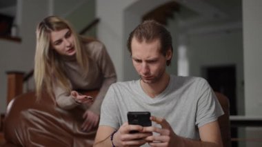 Tacizci bir eş kocasının arkasında durur, o da kanepede oturmuş telefonunu tutuyordur. O, ona bir şey açıklıyormuş gibi hareket ederek ona bakarken, o ciddi bir ifadeyle konuşur. Şey...
