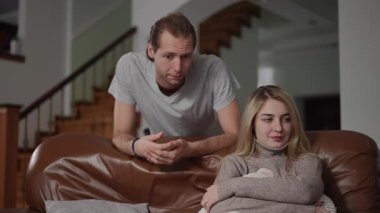 Bir kadın kanepede oturup oyuncak ayıyı tutarken, bir erkek kontrolcü bir şekilde el kol hareketi yapıyor. Bu görüntü kurbanın duygusal ve psikolojik tacizini yansıtıyor.