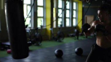 Kendini adamış bir boksör, modern bir spor salonunun içindeki ağır bir torbaya yumruk ve tekme atıyor.