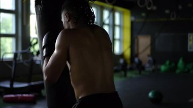 Yetenekli bir boksör, hareketli, dengesiz ve iyi donanımlı bir spor salonunda ağır bir torbaya karşı özenle yumruklarını geliştiriyor.